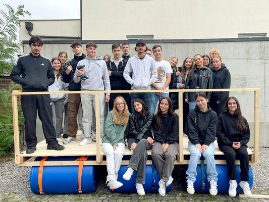 Schülerinnen und Schüler präsentieren stolz ihr selbstgebautes Floß.