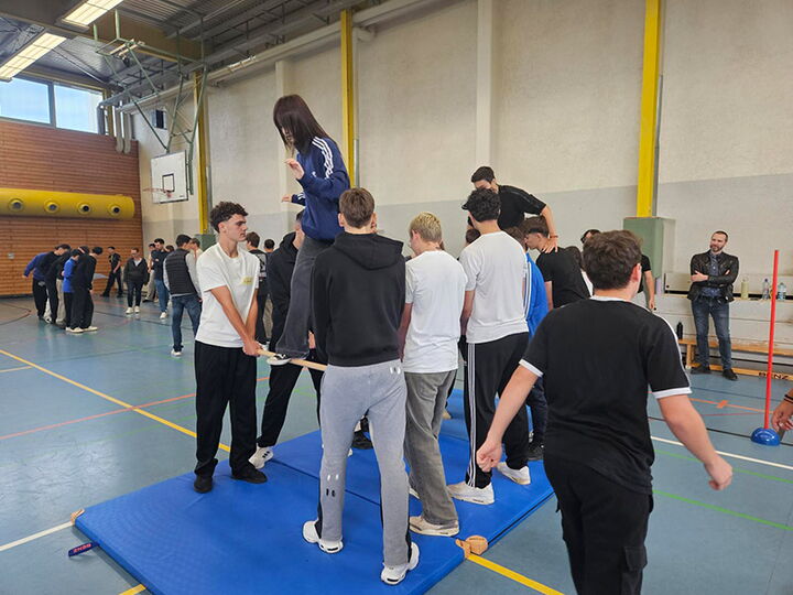 Jugendliche bilden in der Sporthalle bilden eine Brücke aus Stangen, über die ihre Mitschüler balancieren.