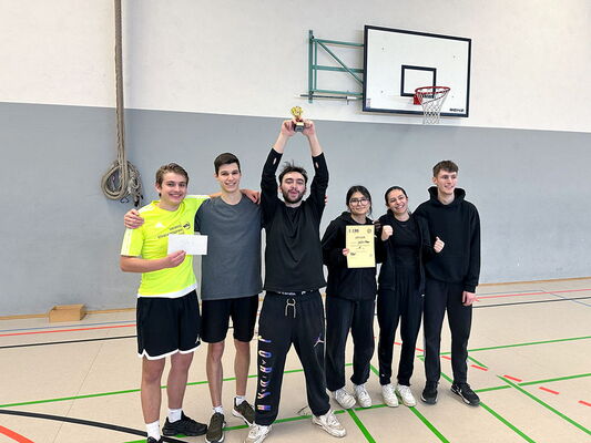 Siegerteam des EBS-Volleyballturniers 2024 posiert jubelnd in der Sporthalle mit Pokal und Urkunde.