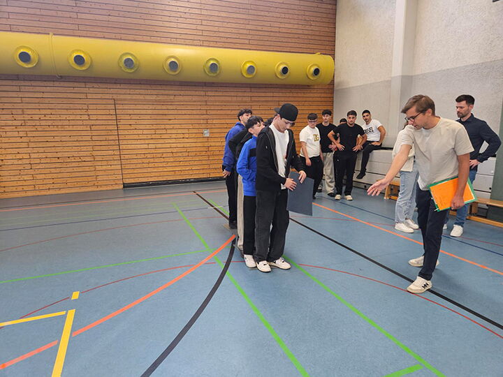 Schüler der Erich-Bracher-Schule stehen hintereinander aufgereiht, während vorne eine Person Anweisungen gibt.