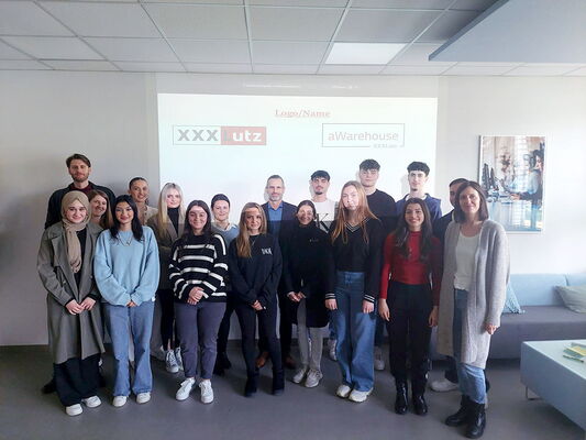 Gruppenfoto von Schülern und Lehrern vor einer Präsentationsfolie mit den Logos von XXXLutz und aWarehouse.