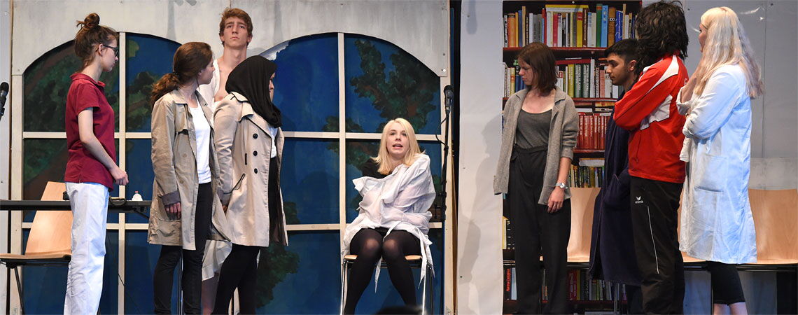 Theaterszene an der Erich-Bracher-Schule: Eine Schülerin sitzt in einer Zwangsjacke auf einem Stuhl, umringt von Mitspielern.
