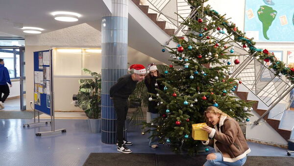 Schüler der EBS entdecken ein Geschenk unter dem Weihnachtsbaum im Foyer der Schule.