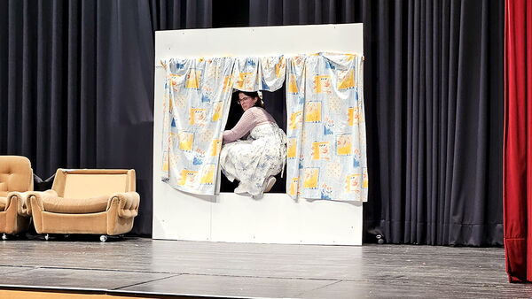 Szene aus dem Theaterstück ‚Lisa im Wunderland‘: Eine Schauspielerin klettert durch ein Fenster mit verspielten Vorhängen.